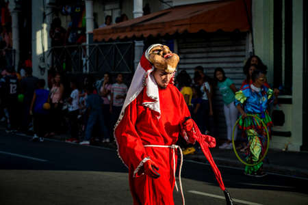 Concepcion De La Vega, DOMINICAN REPUBLIC - FEBRUARY 09, 2020: man in red costume walks by city street full of people dominican carnival on February 9 in Concepcion De La Vegaのeditorial素材