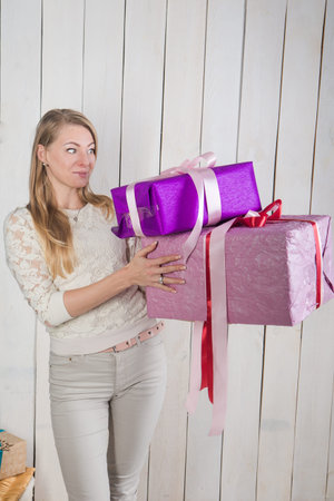 beautiful blonde girl looks with surprise at two large gift boxes holding in hands