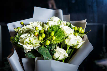 closeup elegant bouquet of big white roses, fresh greenery, and different decorative details served in grey gift craft paperの写真素材