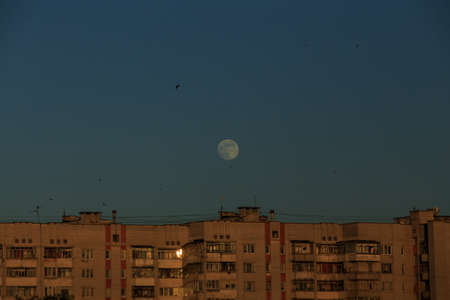 large white full moon on clear blue over an urban high building in evening summertimeの写真素材