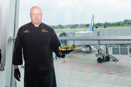 LVIV, UKRAINE - MAY 24, 2018: chef in black uniform hold plate with snacks in Lviv airport hall against arrived airplane on May 24 in Lvivのeditorial素材