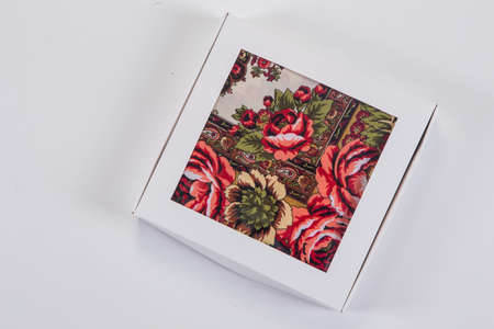 top view on small white gift box with soft cotton scarf with colorful floral ornament designed in flat lay style on light gray backgroundの写真素材
