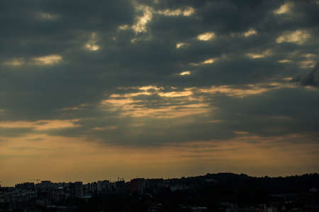 beautiful sunset with heavy gray clouds on dramatic dark sky above large cityscape silhouettesの写真素材