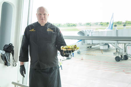 LVIV, UKRAINE - MAY 24, 2018: chef in black uniform holds plate with snacks in Lviv airport hall against arrived airplane on May 24 in Lvivのeditorial素材