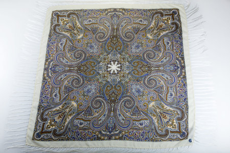 top view flat lay on white cotton scarf with fringe and bright floral ornament with golden, blue and...