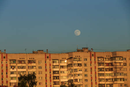 large white full moon on clear blue over an urban city high building in evening summertimeの写真素材
