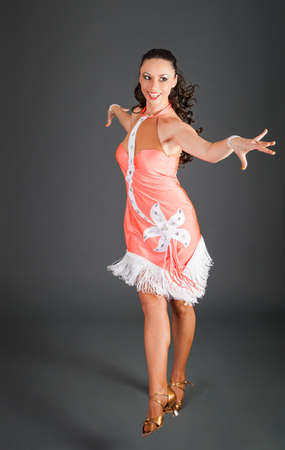 beautiful brunette caucasian girl with curly hair in pink with white inserts dress dances on hight heels on gray background in studioの写真素材