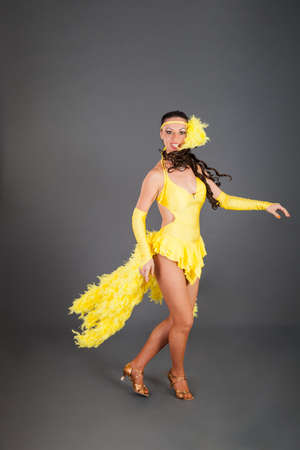 attractive brunette caucasian girl with curly hair in frank yellow suit dances against gray background in studioの写真素材