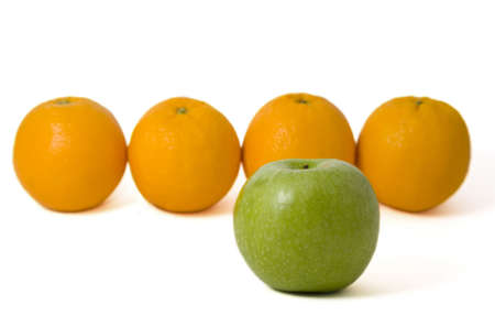 Green apple in front of oranges over white  の写真素材