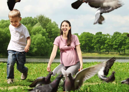 Pregnant woman with her son feeding pigeons in a parkの写真素材