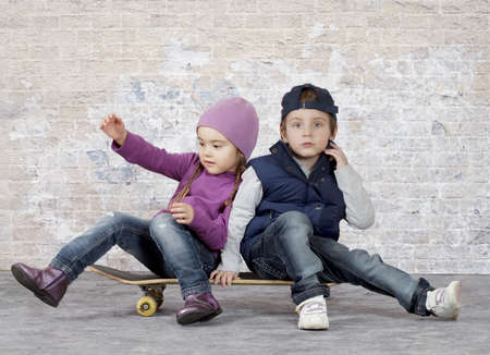 Two little kids sitting on skateboard in front of brick wallの写真素材
