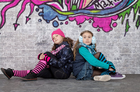Teenage girls sitting in front of brick wall covered with graffitiの写真素材