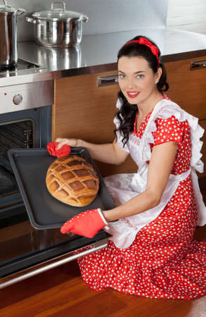 Beautiful brunette housewife holding baking tray with breadの写真素材