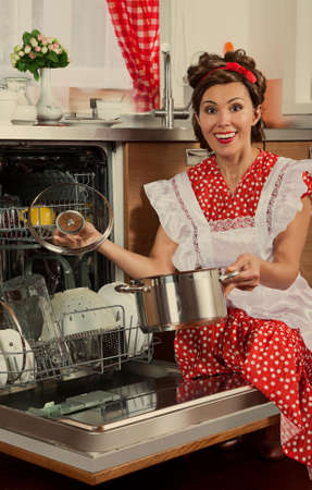 Retro styled housewife loads the dishes in the dishwasher. 1950s style post processing emulation.の写真素材