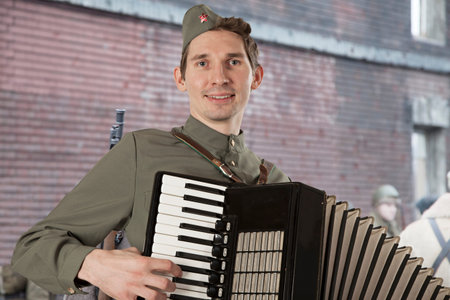Portrait of Soviet soldier in uniform of World War II playing the accordion outdoors