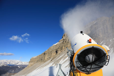 Snow cannon against the blue sky. Snow-making is the production of snow by forcing water and pressurized air through a "snow gun" or "snow cannon", on ski slopesの写真素材
