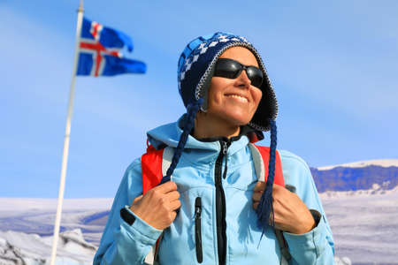Portrait of a young female tourist with backpack on the background of waving Icelandic flag and glaciers, Icelandの写真素材