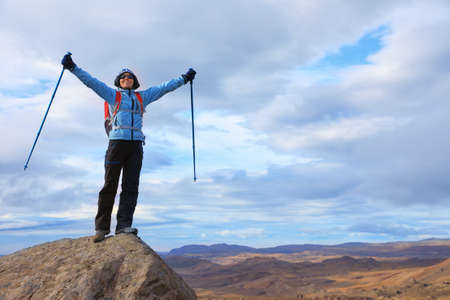 Young woman stands on top of a mountain overlooking the vast expanses of the Icelandic landscapes with arms outstretchedの写真素材