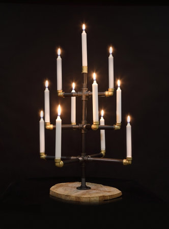 Candlestick made of water pipes in the form of a Christmas tree with lit candles isolated on a black...