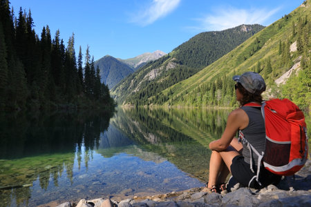 Girl tourist sitting on the shore of lake Kolsay, admiring the stunning views of nature. Kazakhstanの写真素材
