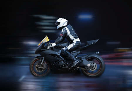 Motorcycle rider in helmet and gear racing at high speed with motion blur on the background of night trackの写真素材