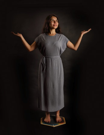 Brunette girl in peace standing on a bed of nails on a black background
