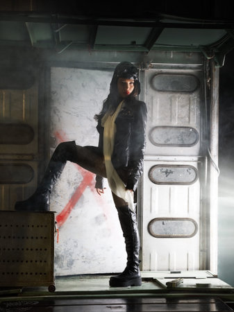 Beautiful brunette girl in the form of a pilot standing in the flight hangar in the sunlight 