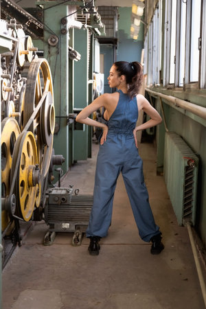 Beautiful brunette girl dressed in overalls posing in the spinning shop in the factory