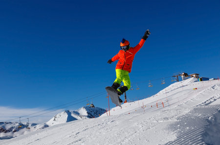Snowboarder jumps from a springboard in a snowpark against a blue sky. Livigno, Italy