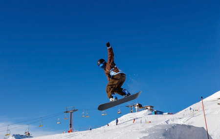 Male snowboarder is jumping with snowboard from snowhill against the blue sky