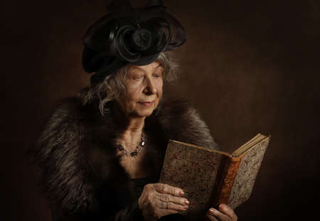Portrait of an old woman with a book in vintage clothes on a brown backgroundの写真素材