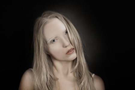 Mysterious conceptual art portrait of a young blonde girl with artistic makeup on a black background