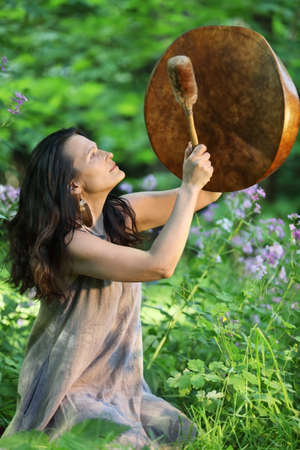 Shaman woman playing her shaman sacred drum in the forest on background with leaves and flowers. Ethnic traditions
の写真素材