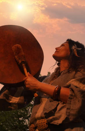 Female shaman performs a ritual with a tambourine at sunset in the forest. Shamanic ritual. Ethnic traditionsの写真素材