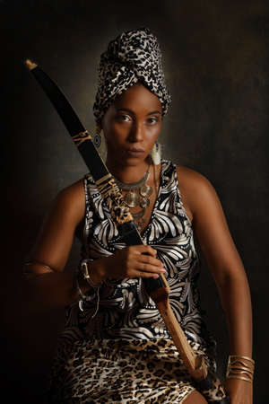 Portrait of a young sensual African American woman in traditional clothes with a bow on an artistic black backgroundの写真素材