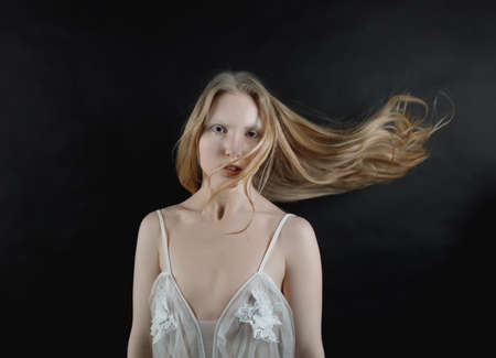 Conceptual art portrait of a young blonde girl with her hair flying on a black backgroundの写真素材