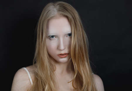 Conceptual art portrait of a young blonde girl with artistic makeup on a black backgroundの写真素材