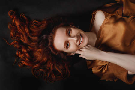 Artistic portrait of a young beautiful red haired woman with a smile on her face on a black backgroundの写真素材