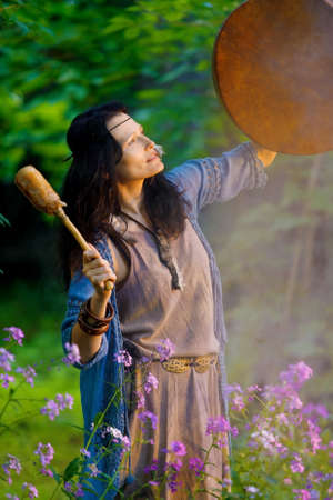 Shaman woman playing her shaman sacred drum in the forest. Ethnic traditionsの素材 [FY310152316102]