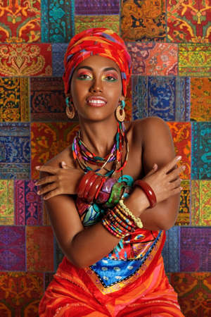 Portrait of a young and attractive African American black woman in the national African clothes against the background of a traditional African carpetの写真素材