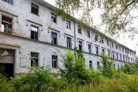 Exterior of an old abandoned hospital building overgrown with grass and greeneryの写真素材