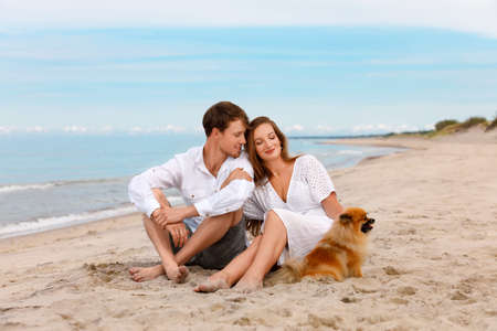 Nice couple of young lovers with a dog relax on the beach on a sunny summer dayの写真素材