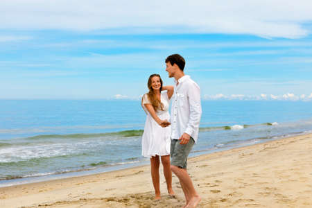 Cute couple of young people in love standing on the sea beach against the blue skyの写真素材