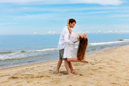 Cute couple of young people in love dancing on the sea beach against the blue skyの写真素材