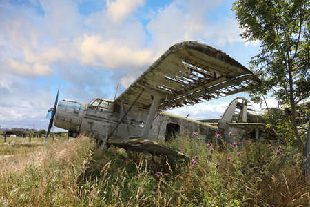 Old crashed and abandoned propeller plane standing in the field against cloudy blue skyの写真素材