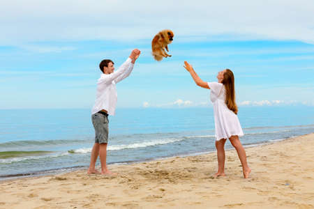 Couple of young people play with their dog on the sea beachの写真素材