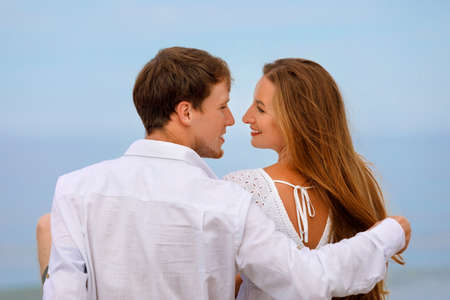 Sweet young couple sitting on the beach and enjoying the view of the sea and each otherの写真素材