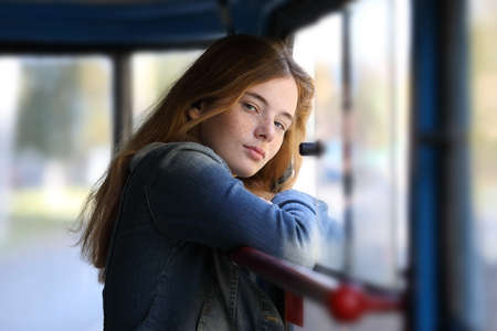 Cute young girl stands at the window of a moving tram and looks at the cameraの写真素材
