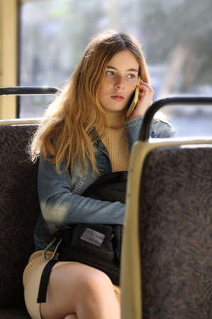 Young cute girl passenger enjoying trip at public transport in modern tram and using mobile phoneの写真素材