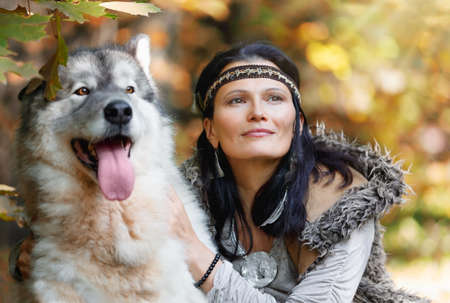 Portrait of a young charming woman with an Alaskan Malamute dog in the autumn forest against the background of natureの写真素材